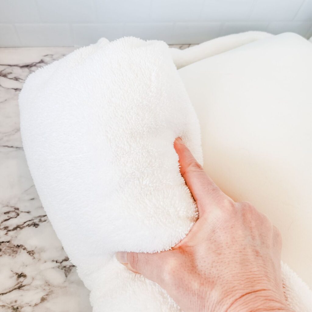 rolling the clean memory foam pillow up in a white towel to dry.