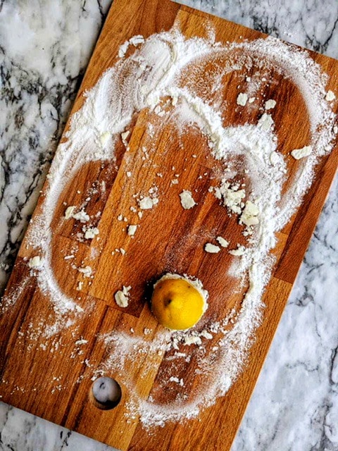 baking soda paste being rubbed with a lemon into a wooden cutting board.