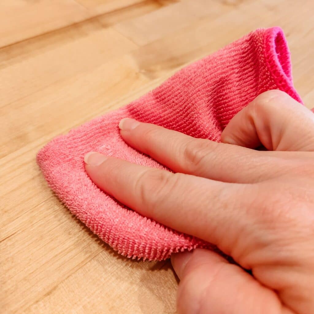 Wiping the excess butcher block conditioner away with a pink towel.