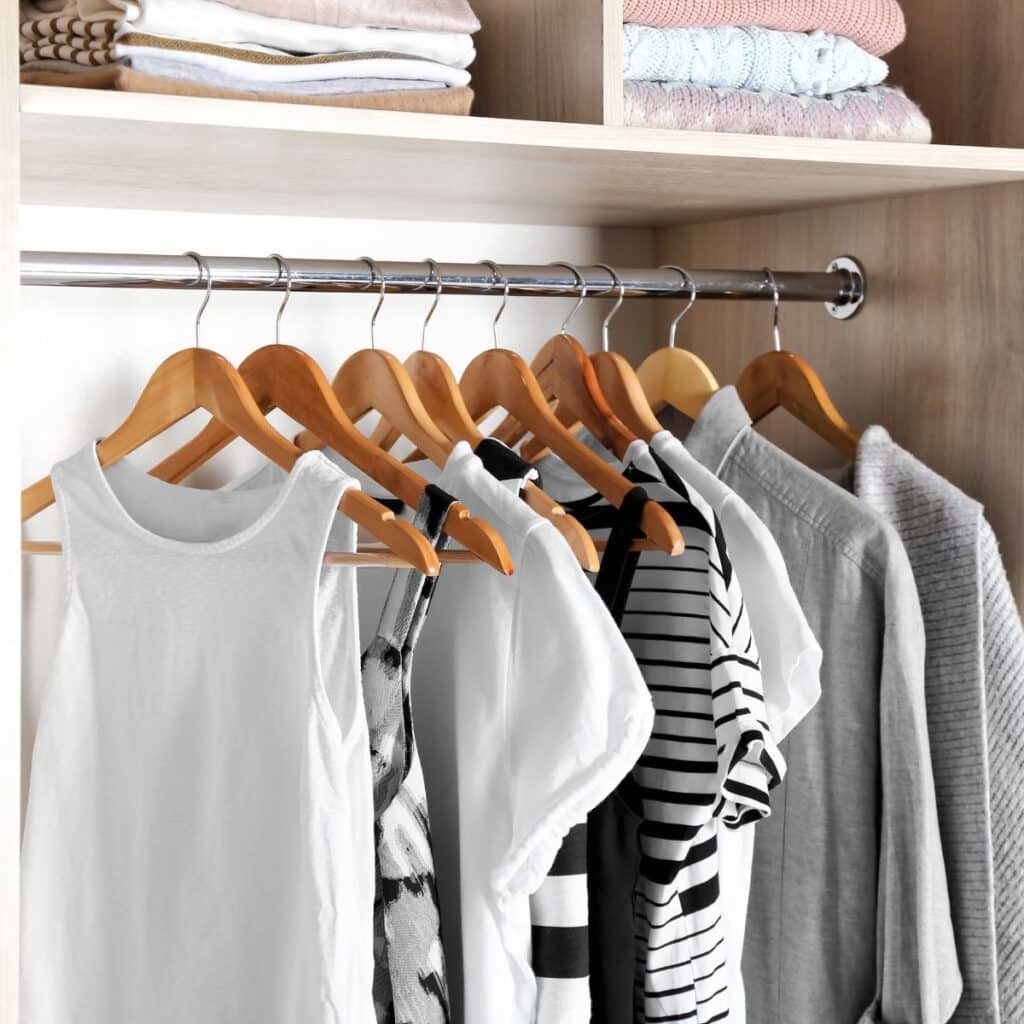 Neatly hung shirts in a closet on wooden hangers.