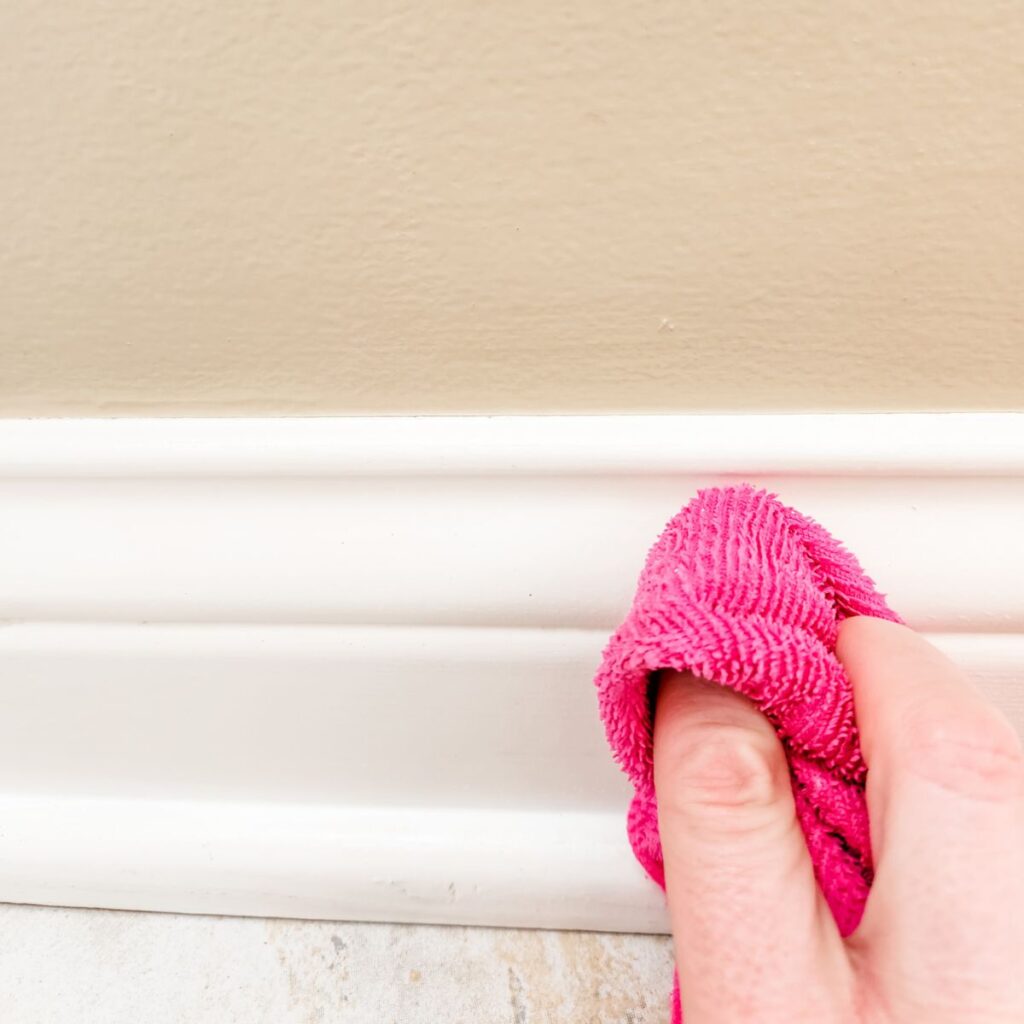 wiping dirty baseboards with a pink microfiber.
